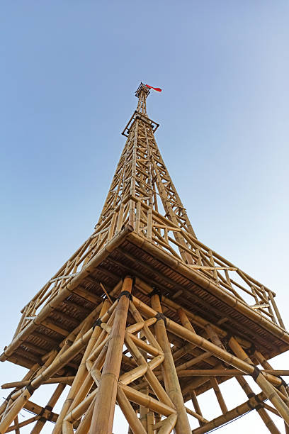 Tuntang, Semarang Regency, Central Java, Indonesia - September 06, 2020: Low angle view of a tall bamboo observation tower topped with the Indonesian flag, photographed against a clear blue sky. The structure showcases traditional bamboo architecture, sustainable construction, and local tourism landmarks.