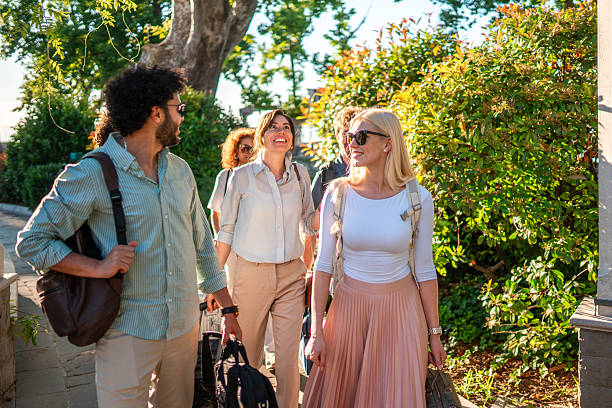 A group of smiling business people engaged in light conversation as they walk outdoors with luggage, displaying a sense of accomplishment and anticipation for their corporate retreat.