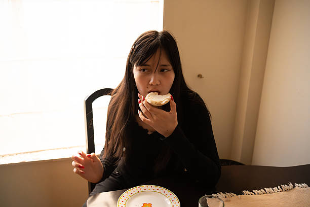 istock Young Woman with Intense Focus Eating Bread at Dining Table 2254312796
