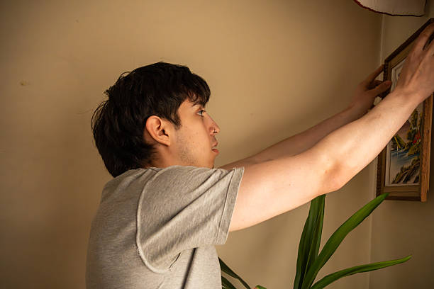 istock Young Man Hanging Picture Frame on Wall in Soft Natural Light 2254312905