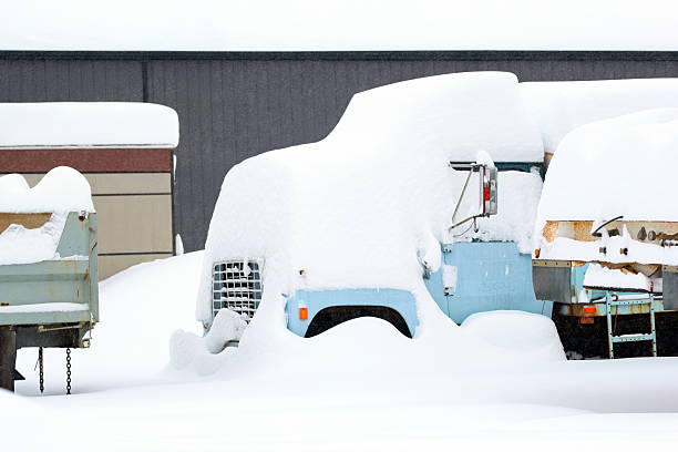 Site with old abandoned dump trucks, metal junk under heavy snow after snowfall in winter, rural landscape.