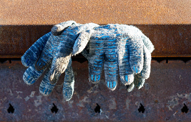 Two blue and gray gloves are hanging on a metal surface. The gloves are dirty and worn. The gloves are not being used