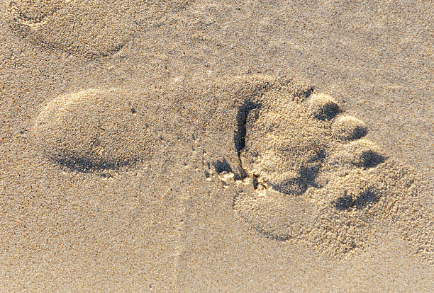 A foot print is in the sand. The sand is white