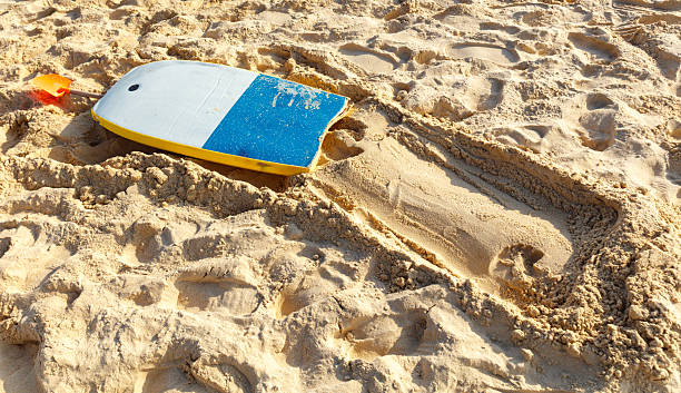 A surfboard is laying on the sand. The surfboard is blue and yellow