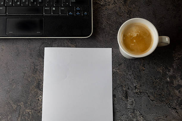 Top view of a minimalist home office workspace featuring a laptop, coffee cup, and blank paper with copy space. The image represents remote work, productivity, modern work culture, and everyday professional life in a clean, neutral setting.