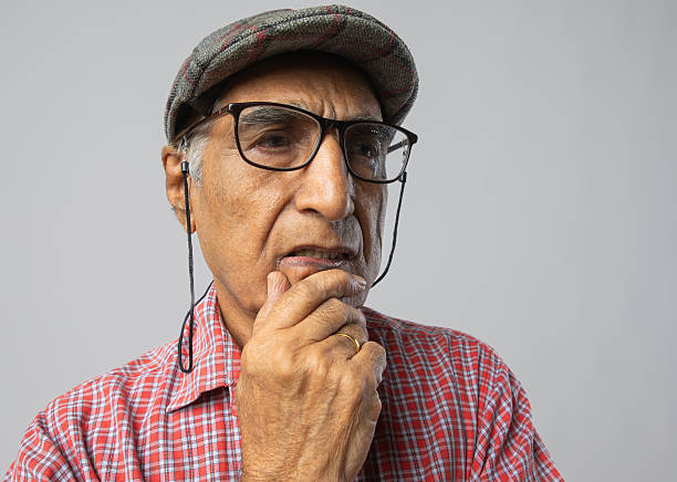 Close-up portrait of serious senior man in eyeglasses and cap looking away thoughtfully against white background