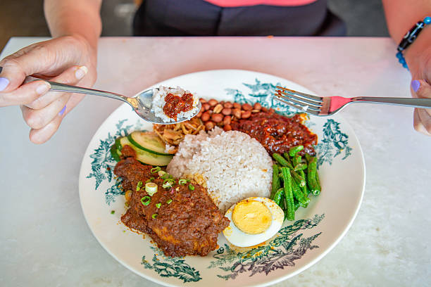 unrecognizable woman eating Malaysian Nasi Lemak in restaurant with Rendang Chicken, egg and sambal chili