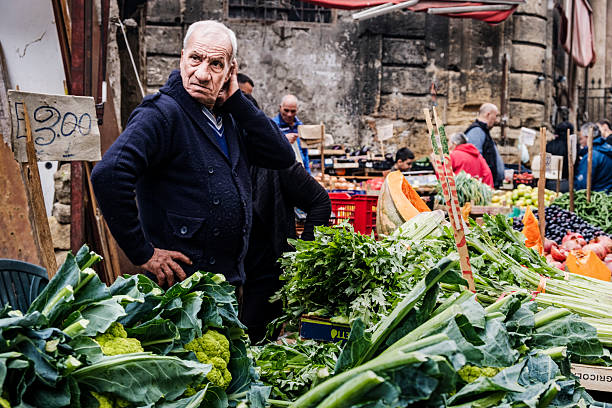 Ballaro Market, Palermo, Sicily, Italy 11/19/2025. Candid street scene from Ballaro Market in Palermo as the stallholder watches over hisfruits and vegetables as customers walk by.