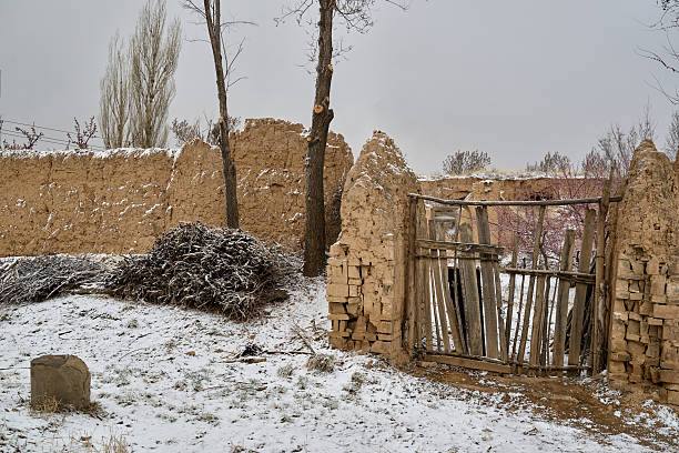 Abandoned mud-brick settlement with traditional gateway in snowy mountain valley