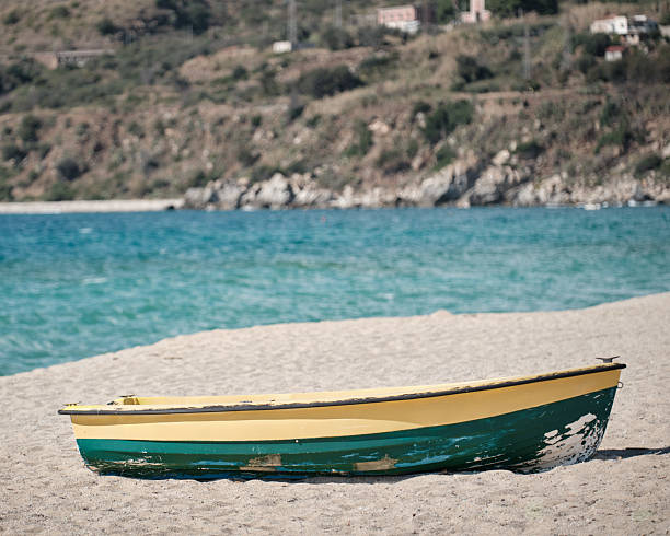 Wooden boat on sandy beach with turquoise sea and rocky coastline, featuring open space above ideal for travel covers, marketing visuals and holiday themes.