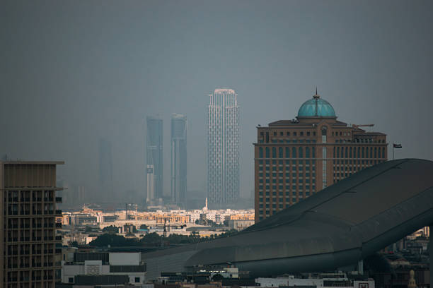 A distant view of the Dubai skyline photographed through warm desert haze. Modern skyscrapers and distinctive architecture rise above the city, including the curved roof of Ski Dubai in the foreground. A cinematic and atmospheric urban travel image from the United Arab Emirates.
