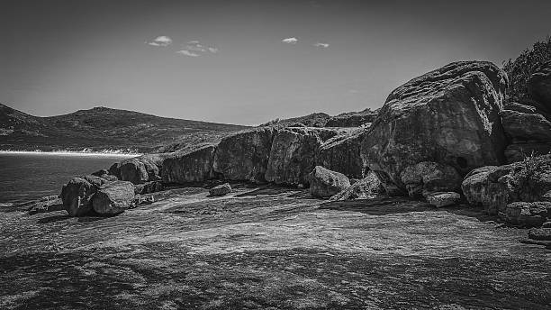 A striking black and white seascape showcases a rugged coastline, weathered rocks, and a serene ocean under a clear sky.