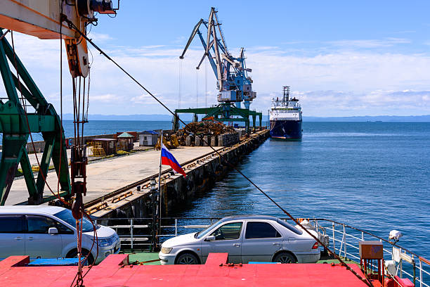 Korsakov, Russia - August 30, 2025: Vessels are docked at the Kazanin port, with cranes preparing for cargo loading under a vibrant sky. Cars line the pier as activity fills the scene with purpose.