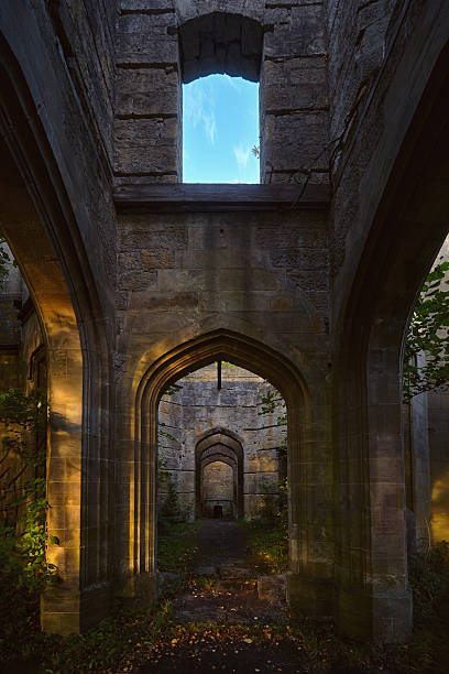 Interior view of Dunmore House ruins in Scotland. Arched stone doorways and soft evening light illuminating ancient walls with plants growing inside the abandoned building.