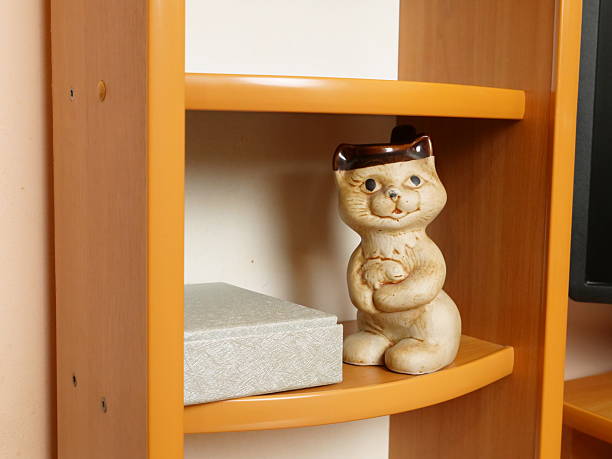 Ceramic cat figurine on wooden shelf next to box. Home interior with decorative vintage accent.