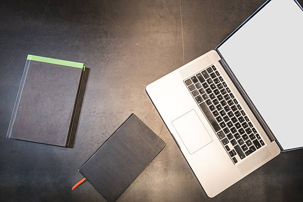 Top view of an open laptop and two books placed on a table. Minimal workspace setup representing education, remote work, online learning, research, and productivity.
