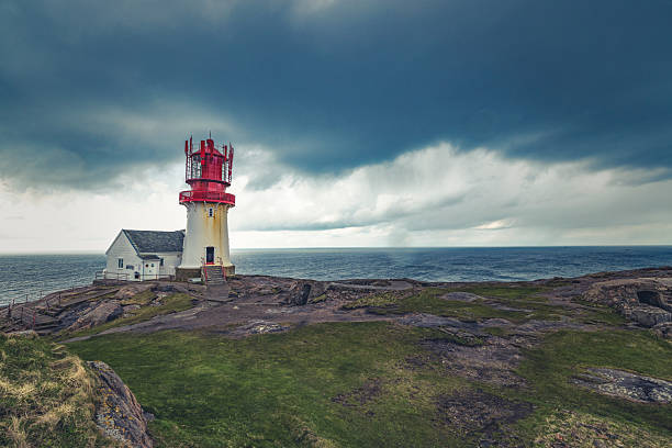 Lindesnes Lighthouse on a rocky coastline under dark storm clouds, overlooking the North Sea at the southernmost point of Norway. Dramatic weather and rugged Scandinavian landscape.