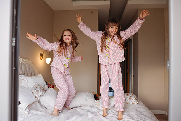 istock Two young sisters are jumping on a bed, having fun and enjoying their time together. 2254343688