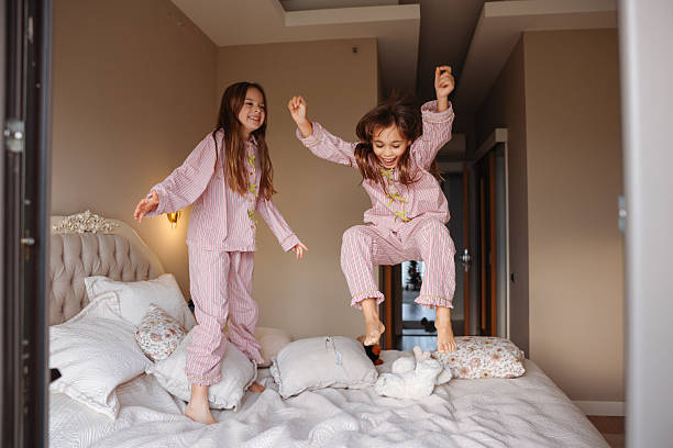 istock Two young sisters are jumping on a bed, having fun and enjoying their time together. 2254343723