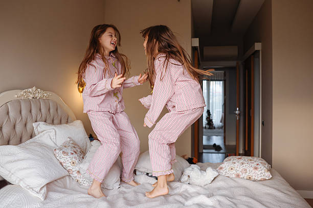 istock Two young sisters are jumping on a bed, having fun and enjoying their time together. 2254344627