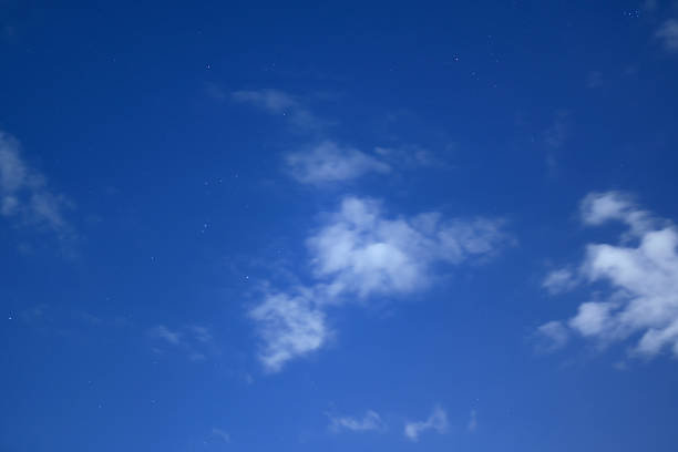 A serene and atmospheric night sky scene where a soft layer of white clouds partially veils the deep blue celestial expanse. Faint stars glimmer through the misty haze, creating a sense of calm, mystery, and cosmic depth. This shot captures the ephemeral beauty of the night during a quiet astronomical observation.