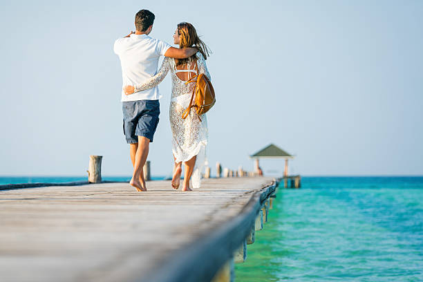 Young couple walking embraced along jetty at Dhiffushi Holiday island, South Ari atoll, Maldives. Model and Property released. Hi resolution photo.