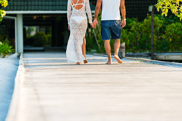 Young couple walking holding hands along jetty at Dhiffushi Holiday island, South Ari atoll, Maldives. Model and Property released. Hi resolution photo.