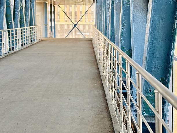 Empty Steel Pedestrian Bridge With Strong Perspective And Converging Beams, Industrial Interior Bathed In Cool Light, Repeating Railings And Grid Ceiling, Clean Minimalist Mood Suited