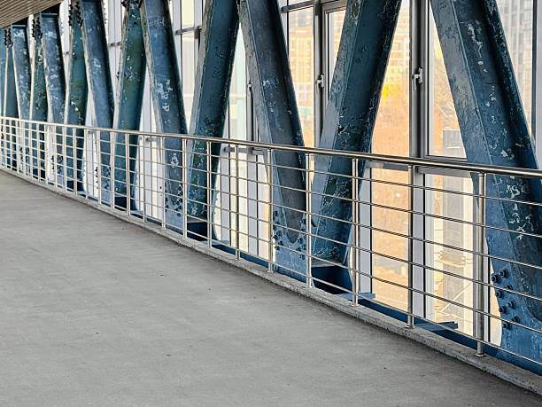 Empty Steel Pedestrian Bridge With Strong Perspective And Converging Beams, Industrial Interior Bathed In Cool Light, Repeating Railings And Grid Ceiling, Clean Minimalist Mood Suited