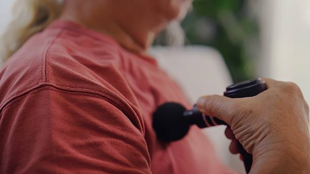 istock Elderly Asian Man Using Massage Gun While Checking Smartphone at Home. 2254354220
