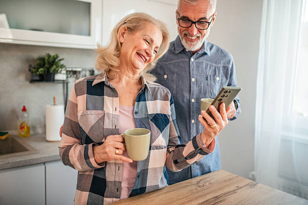istock Smiling mature couple drinking coffee and watching smartphone in kitchen 2254354852