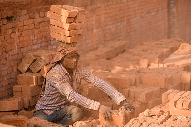 Migrant laborers balance bricks on their heads at a brick kiln in Bhaktapur, Nepal. Seasonal laborers from various parts of Nepal and India arrive during the winter season to work at kilns.