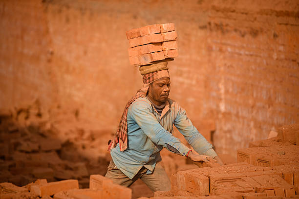 Migrant laborers balance bricks on their heads at a brick kiln in Bhaktapur, Nepal. Seasonal laborers from various parts of Nepal and India arrive during the winter season to work at kilns.