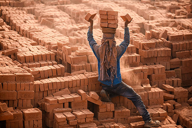 Migrant laborers balance bricks on their heads at a brick kiln in Bhaktapur, Nepal. Seasonal laborers from various parts of Nepal and India arrive during the winter season to work at kilns.