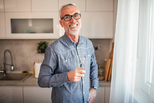 istock Portrait of a mature man with eyeglasses refreshing himself by drinking water by the window 2254355708