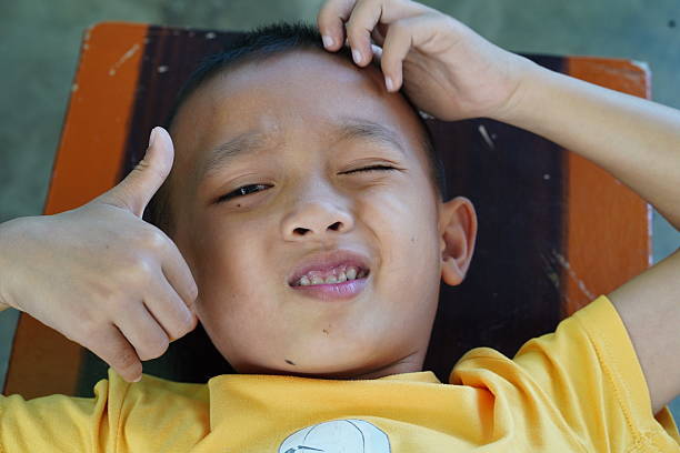 Young boy expressing mixed emotions while lying down, giving a thumbs up with a playful smile in a cheerful setting, perfect for family or childhood themes