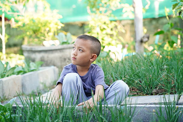 A young boy sits peacefully on the grass in a serene garden, reflecting quietly amidst lush greenery, capturing the essence of childhood innocence and tranquility.