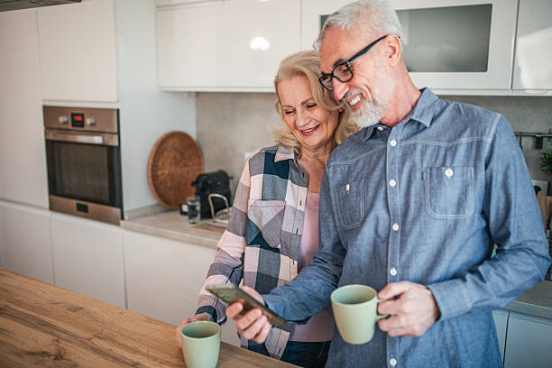 istock Happy senior couple drinking coffee and watching smartphone in kitchen 2254356423