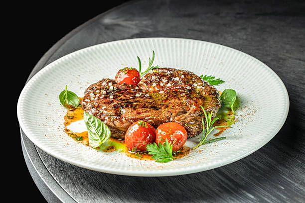 istock Grilled pork steak with herbs and cherry tomatoes served on white plate on dark table 2254356681