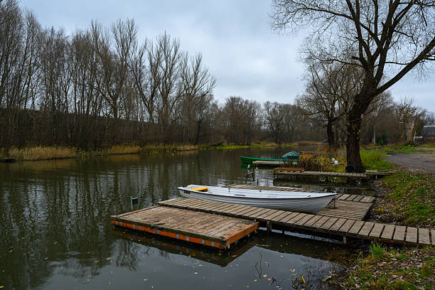 Pereslavl-Zalessky, Russia - November 4, 2025: A serene dock rests by the quiet waters of a river in Pereslavl-Zalessky, with a small boat tied up and autumn trees reflecting in the calm surface.