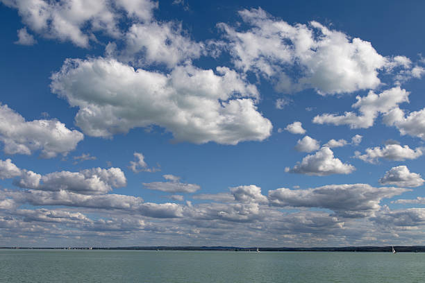 A scenic view of a bright blue sky filled with puffy white clouds, overlooking a calm body of water.