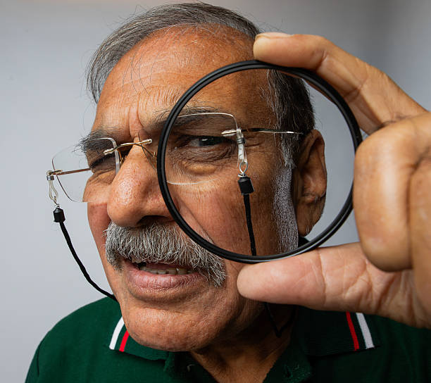 Close-up suspicious senior detective in eyeglasses looking through magnifying glass against white background