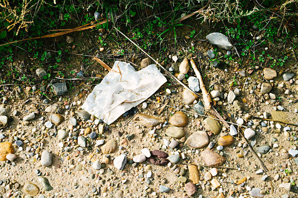 Discarded wet wipe lying on natural ground near a reservoir. Concept of pollution, waste, environmental damage, and human impact on nature