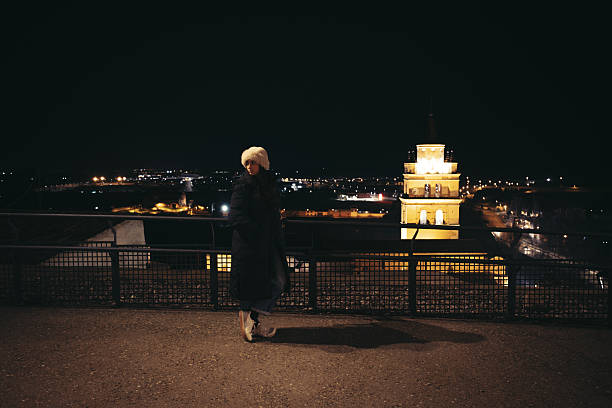 A person standing outdoors at night overlooking illuminated city buildings, conveying urban lifestyle, night atmosphere, travel, and contemplation.