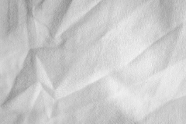Detailed view of crumpled white paper with visible creases and soft wrinkles creating a dynamic, uneven surface. The light grey tones and rough texture suggest imperfection and spontaneity.