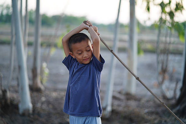 istock Young boy stretches with stick in rural setting, surrounded by trees and open fields. scene captures moment of playfulness and tranquility in nature 2254363939