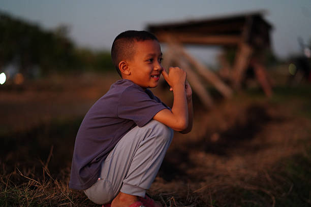 Young boy sits thoughtfully in serene outdoor setting during sunset, showcasing moment of contemplation and joy. warm light enhances peaceful atmosphere