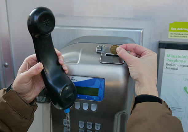 Vienna, Austria - 26 December 2025: Man using public payphone, inserting coin into payment terminal. Urban communication technology, telecom service, travel, customer service, vintage phone concept.