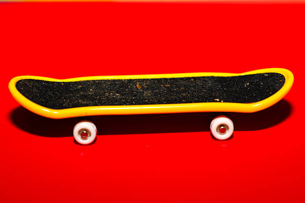 A bright yellow toy fingerboard with a black deck and white wheels is positioned against a rich red background. This miniature skateboard model symbolizes modern teenage hobbies,