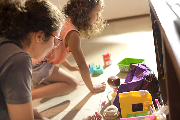 Young mother watching her daughter play with toys on the floor, representing care, attention, family bonding, and childhood development.
